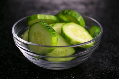 Siyah bir arka planda şeffaf bir tabakta dilimlenmiş salatalık. Yakın plan..