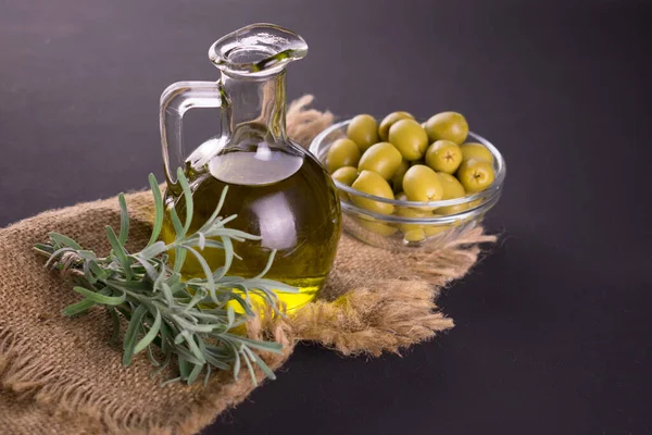 Olive oil in a bottle and fresh rosemary on a dark background.