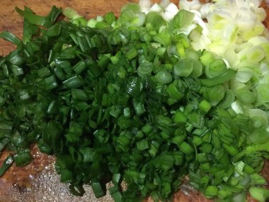 Mutfakta bir ahşap masada ıslak yeşil soğan kesin. Bahar salatalarında çok faydalı.