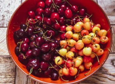 Ahşap arka planda turuncu bir tabakta farklı türde tatlı kirazlar.