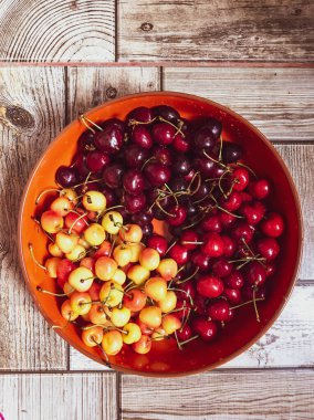 İskoç kedisi, ahşap bir arka planda turuncu derin tabakta farklı türde tatlı kirazlar.
