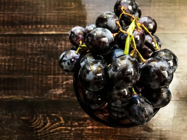 Tahta bir masanın üzerinde şarap ve üzüm dolu bir bardak.