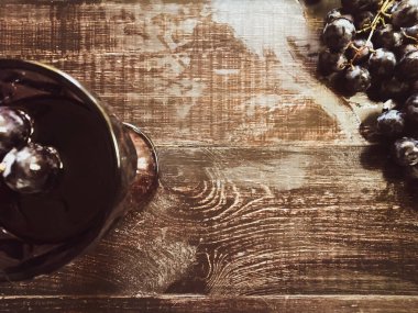 Tahta bir masanın üzerinde şarap ve üzüm dolu bir bardak.
