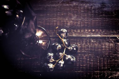 Tahta bir masanın üzerinde şarap ve üzüm dolu bir bardak.