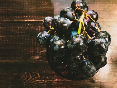 Tahta bir masanın üzerinde şarap ve üzüm dolu bir bardak.