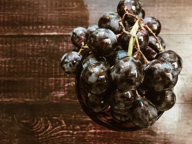 Tahta bir masanın üzerinde şarap ve üzüm dolu bir bardak.