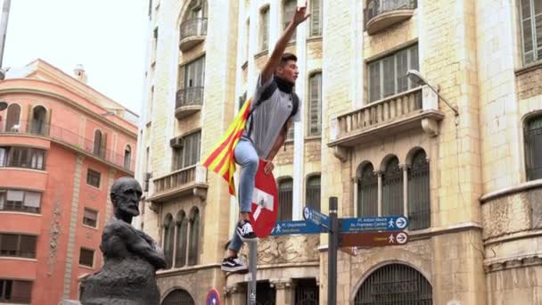 Guy with catalonia flag sits on road sign during protests on barcelona street — ストック動画