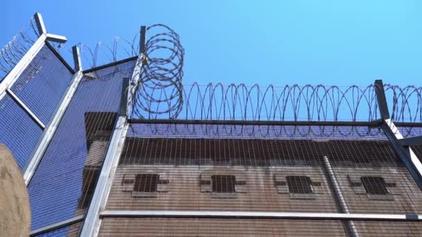 Pared del edificio de la prisión con pequeñas ventanas con barras y una valla alta — Vídeos de Stock