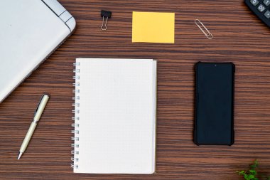 Ortamda çalışan bir ofis masası. Not defteri, yapışkan not, kalem fabrikası, hesap makinesi ve kahverengi çizgili zebra tahtası dizayn sehpasında bir laptop. Covid-19 sırasında evde çalışırken nesneler olmalı.