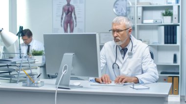 Bir üst düzey doktor ve onun yardımcısı çalışma masaüstü bilgisayarlar konusunda yakın çekim shot. Parlak oturan Office yaktı.