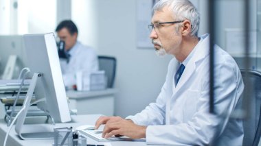 Masaüstü bilgisayarını ofisinde çalışan üst düzey tıp doktoru. Ayrıca asistanı arka planda çalışır.