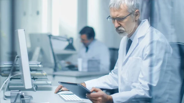 Médico Sénior Practitioner Sentado Antes Computador Pessoal Usa Tablet Computer — Fotografia de Stock