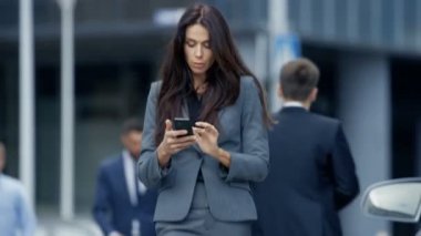 İş kadını iş bölgesinde yoğun büyük şehir cadde üzerinde yürüyen özel takım elbiseli onun Smartphone denetler. Her şekilde, büyük iş yapmak emin kadın.