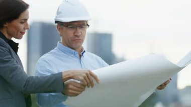Proje iş kadın yatırımcı taslaklara şef mühendis gösterir. Gökdelenler ile arka plan şehirde.