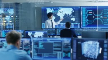 Sistem kontrol odasında baş mühendis bir brifing personel üyesi için tutar. Onlar veri merkezinde iş ve birden çok ekran gösteren haritalar tarafından lojistik veri çevrilidir.