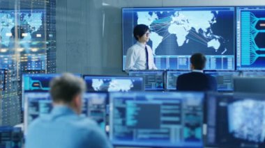Sistem kontrol odasında Yöneticisi bir brifing onun personeli için tutar. Onlar veri merkezinde iş ve birden çok ekran gösteren haritalar tarafından lojistik veri çevrilidir.