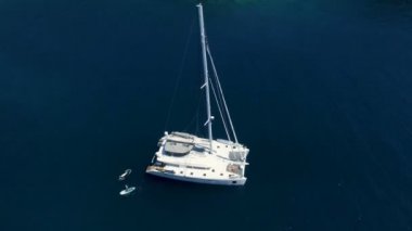 Havadan Top bir büyük beyaz Yelkenli Yat demirlemiş bir Bay adam Standup Paddleboarding yakınındaki ile atış aşağı bu. Okyanusu koyu mavi ve güzel olduğunu.