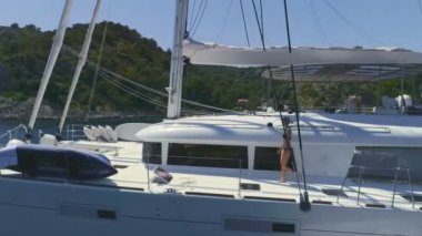 Sevgili güneş banyosu için katılmadan yat güverte yelken beyaz üzerinde yürüyen bir kadın hava atış takip. Güzel Rocky yeşil sahil görünür olduğunu.