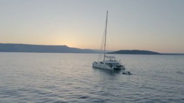 Bir Yelkenli tekne ile Sailes sakin denizde hareket aşağı hava atış. Güzel sahil ve akşam / erken sabah gökyüzü görünür.