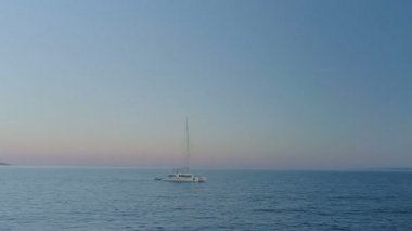 Sakin deniz Hills sahil görünür ile seyahat eden bir beyaz Yelkenli Yat hava hızlandırılmış Arc vurdu. Sabah / akşam.