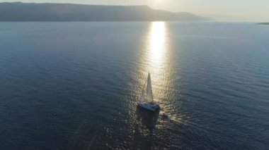 Bir yelkenli katamaran yat yükseltilmiş Yelkenli açık denizler seyahat hava görünümünü. Kıyı Hills görünür güneş parlıyor.
