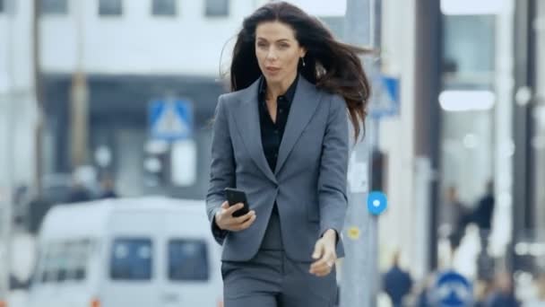 ビジネス地区の忙しい大都市通りを歩いてテーラード スーツでビジネスの女性は 彼女のスマート フォンをチェックします ビッグ ビジネスを行うに彼女の方法に自信を持って女性 — ストック動画