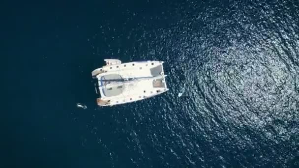 空中顶向下射击一艘大型的白色帆船停泊在一个海湾与男子站立冲浪附近 海洋是深蓝色和美丽的 — 图库视频影像