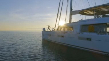 Hava atış üç güzel uygun kadınların bir beyaz yelkenli katamaran tekne sabah Yoga yapıyor. Rising Sun ile huzurlu deniz.