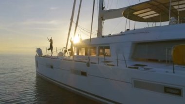 Hava atış üç güzel uygun kadınların bir beyaz yelkenli katamaran tekne sabah Yoga yapıyor. Rising Sun ile huzurlu deniz.