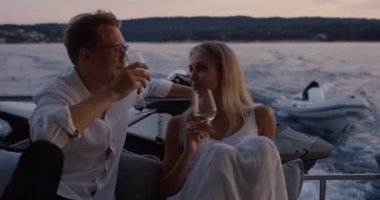 Genç çift konuşma, hareketli yat kıçta şampanya iç. Büyük romantik akşamlar. Küçük köy ile arka plan Island'da.
