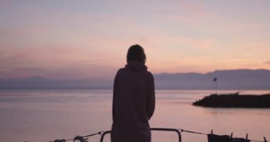 Şık genç kız koyar Hoodie yayından yat'ın güzel pembe gün batımını izlerken iken.