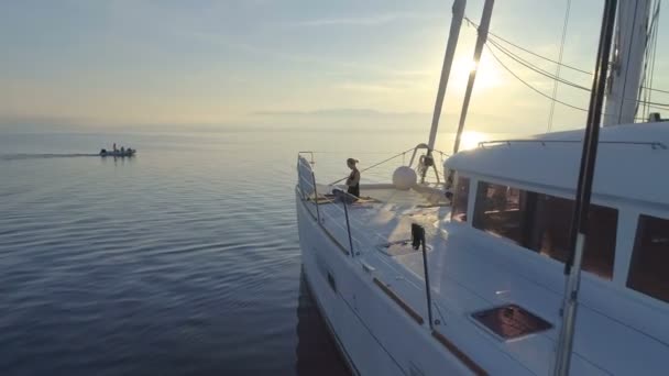 つの美しいの空中ショットに合わせて白い帆船カタマランで朝ヨガをしている女性 昇る太陽と穏やかな海 — ストック動画