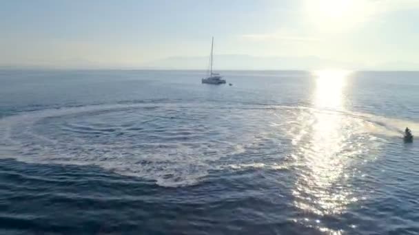 鸟瞰白色帆船双体船和喷气滑雪车在附近盘旋 美丽的天气与平静的镜子像大海和阳光照耀 — 图库视频影像
