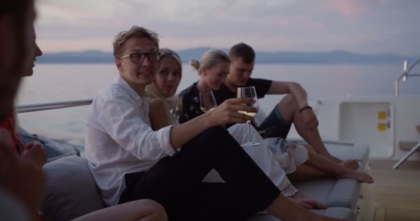 一群年轻人说话 在移动游艇的船尾喝香槟 他们有很好的假期 在背景岛屿与小村庄 — 图库视频影像