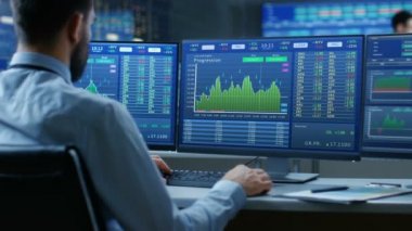 Borsa Tüccarının Omuz Görünümü üzerinde Çoklu Monitörler ile çalışan Borsa Numarası ve Grafikleri Gösteren Bir Bilgisayar.