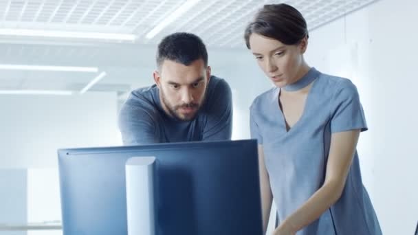 男性と女性のオフィス ワーカーは パーソナル コンピューターに表示される情報を議論します 事務所はモダンで明るい — ストック動画