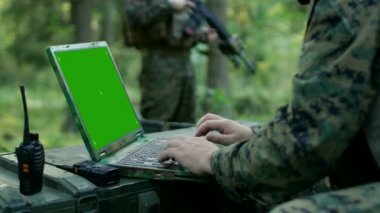 Yakın çekim asker kullanır askeri sınıf Laptop ile yeşil perde. Askeri üste ormanın içinde arka planda kamufle.