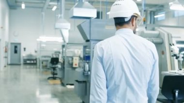 Arkadan görünüm görüntülerini dizüstü tutarak hafif Modern fabrikası ile yürüyüş zor şapka şef mühendis. Modern sanayi ortamında başarılı, yakışıklı adam.