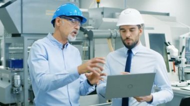 Bölüm Başkanı Laptop tutar ve ürün ayrıntıları şef mühendis ile anlatılır. Onlar giymek zor şapka ve Modern fabrikada iş. Orta atış.