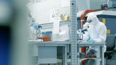 İki mühendis / bilim adamları / teknisyenleri steril elbiseli mikroskoplar araştırma için kullanın. Fabrika üretim bir elektron komponentler çalışıyorlar.