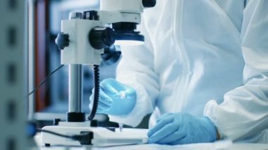 Yakın çekim mühendisi / teknisyen / bilim adamı kontrol elektronik komponent mikroskop altında. Steril Coverall takım elbise ve koruyucu gözlük fabrika üretim elektronikte çalışırken giyer.