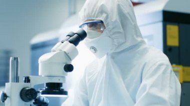 Yakın çekim mühendisi / teknisyen / bilim adamı kontrol bileşen mikroskop altında. Steril Coverall takım elbise ve koruyucu gözlük bir proje çalışırken giyer.