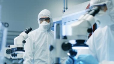İki mühendis / bilim adamları / teknisyen steril temiz oda takım elbiseli kontrol makine çalışma imalat ve mikroskoplar bileşen ayarı ve araştırma için kullanın. Onlar bir elektron komponentler fabrika üretim iş.
