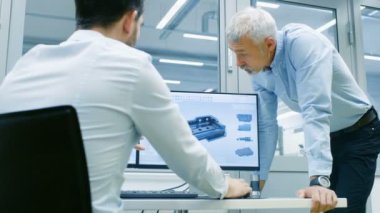 Endüstriyel tasarımcı konuşma Kıdemli mühendis ile yeni bileşen tasarımı Cad programında çalışırken vardır. O inşaat üstünde kişisel bilgisayar ile iki monitör.