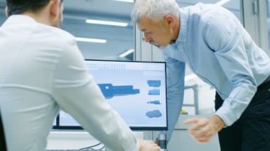 Endüstriyel tasarımcı konuşma Kıdemli mühendis ile yeni bileşen tasarımı Cad programında çalışırken vardır. O inşaat üstünde kişisel bilgisayar ile iki monitör.
