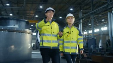 Cep telefonu ve ağır sanayi ile fabrika üretim yürürken tartışma mühendis kadın ile erkek Proje Yöneticisi. Büyük metal yapılar, boru hattı öğeleri etrafında yalan.