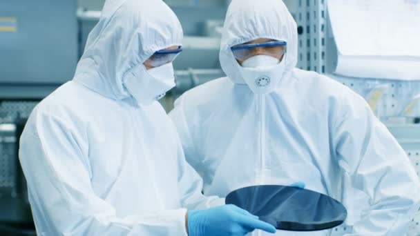 つのエンジニア 科学者 技術者滅菌スーツに半導体用シリコンウェーハをチェックします 彼らは最新の半導体製造工場で働く — ストック動画
