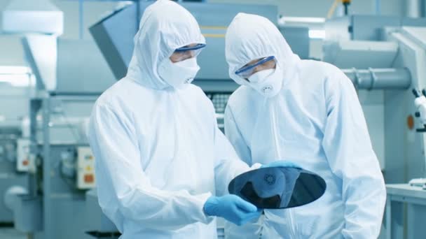 两名工程师 科学家 技术员在无菌西装持有半导体硅片 将制造成电脑芯片 他们在现代半导体制造工厂工作 — 图库视频影像