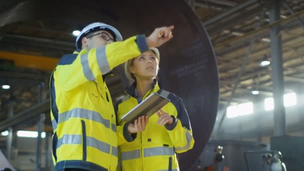 Ingénieurs industriels masculins et féminins dans Hard Hats Discuter nouveau projet tout en utilisant Tablet Computer. Ils travaillent dans une usine de fabrication d'industrie lourde .