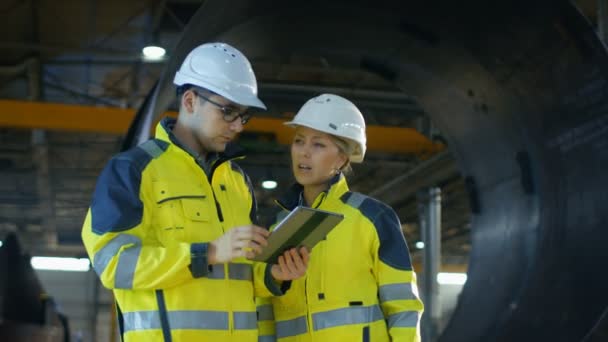 Ingénieurs industriels masculins et féminins dans Hard Hats Discuter nouveau projet tout en utilisant Tablet Computer. Ils prennent des décisions d'ingénierie calculées.Ils travaillent dans une usine de fabrication de l'industrie lourde .